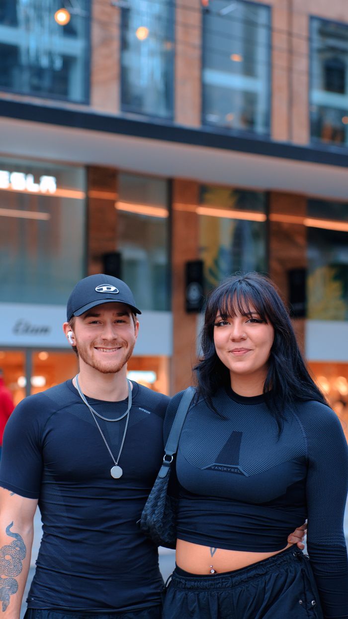 Stylish young couple smiling in urban setting wearing sportswear and accessories.