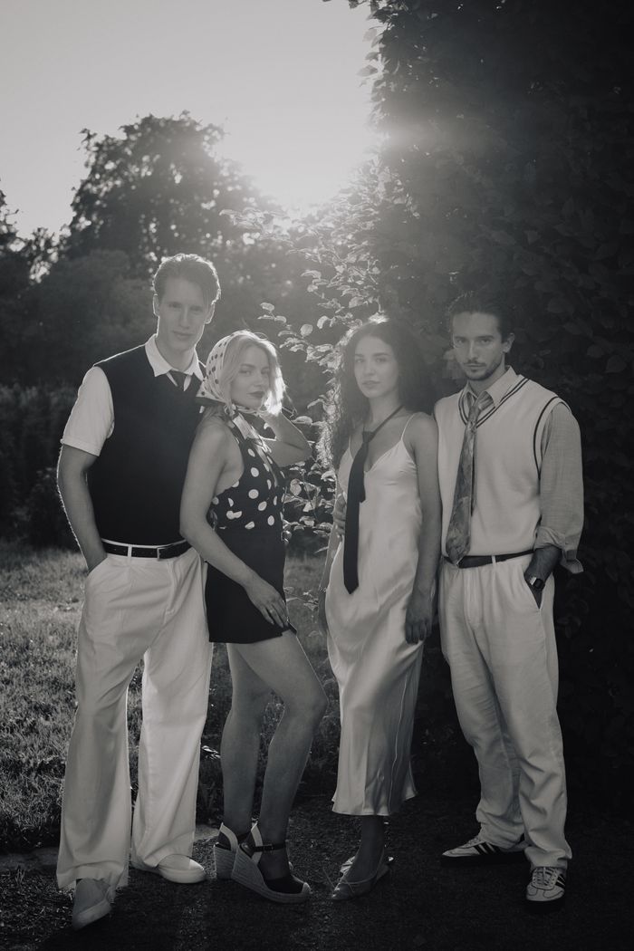 Black and white photo of four adults in vintage attire posing outdoors at sunset.