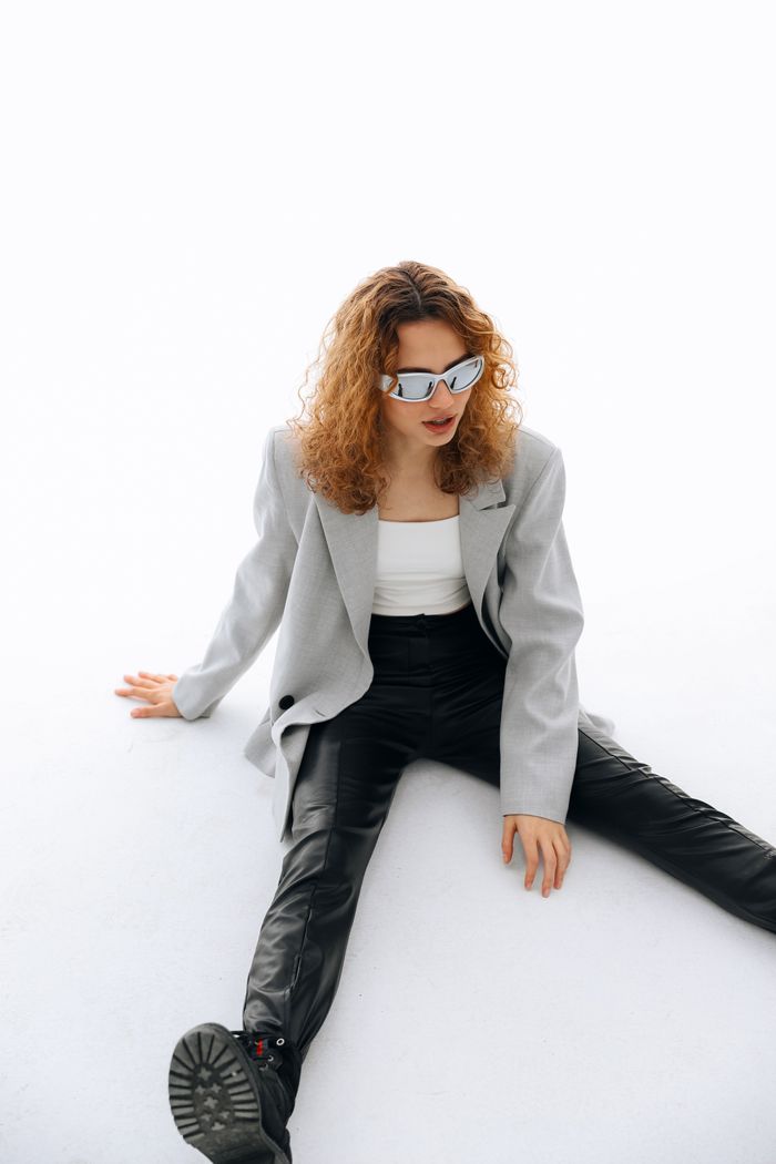 services-01 Woman in trendy outfit sitting on white floor, wearing edgy sunglasses for fashion look.