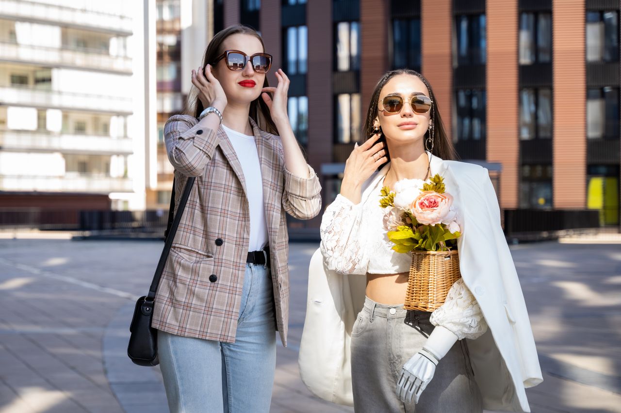 heros-img Two stylish women enjoy a sunny day in the city wearing chic outfits and sunglasses.